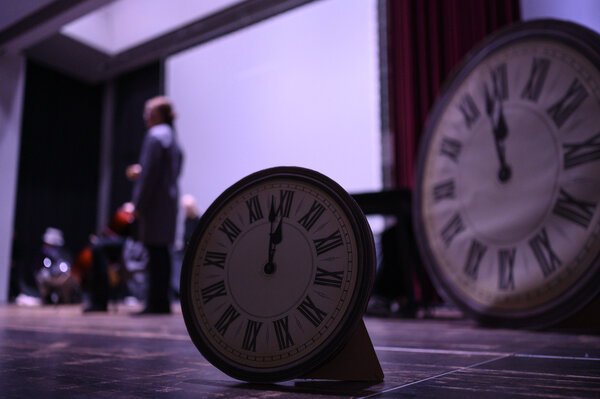 große Uhr auf der Bühne mit Schauspieler im Hintergrund